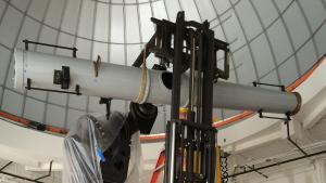 Large white telescope on heavy metal pier with man on ladder and others standing below as they  work on it.