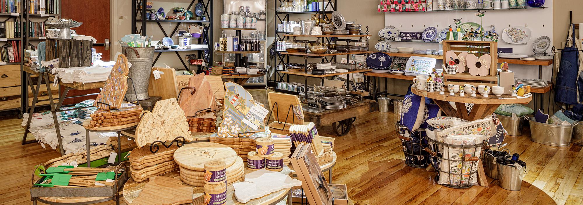 Space with wooden floors, tables and shelves full of houseware products (cutting boards, plates, cups, etc) with South Carolina imagery including crescents and palmetto trees
