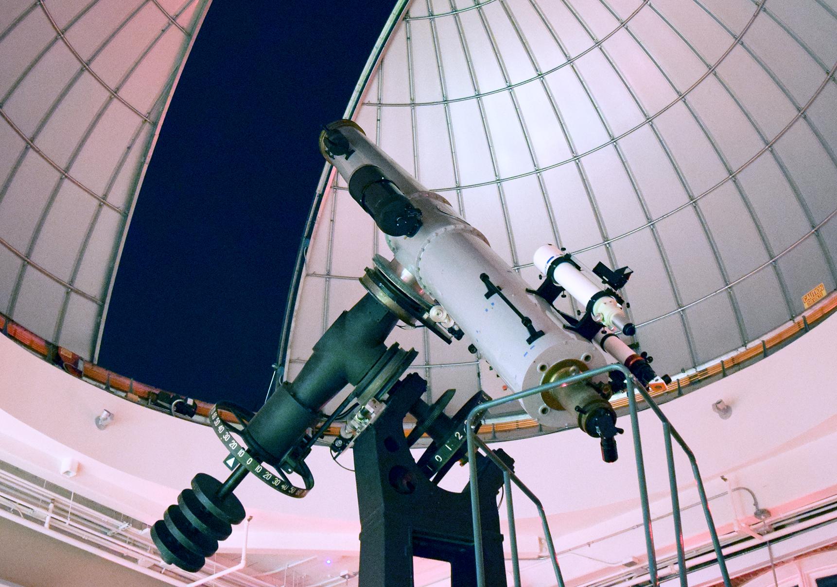 Large white telescope points towards the dark night sky under a partially open observatory