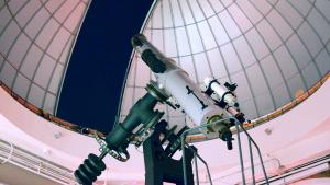 Large white telescope points towards the dark night sky under a partially open observatory