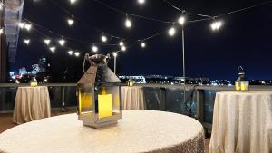 Terrace at night with skyline visible in background and string lights set up above three formally set tables