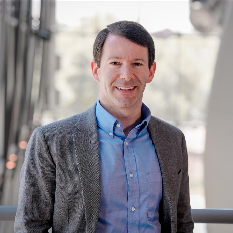 Man in gray suit jacket and blue shirt smiles