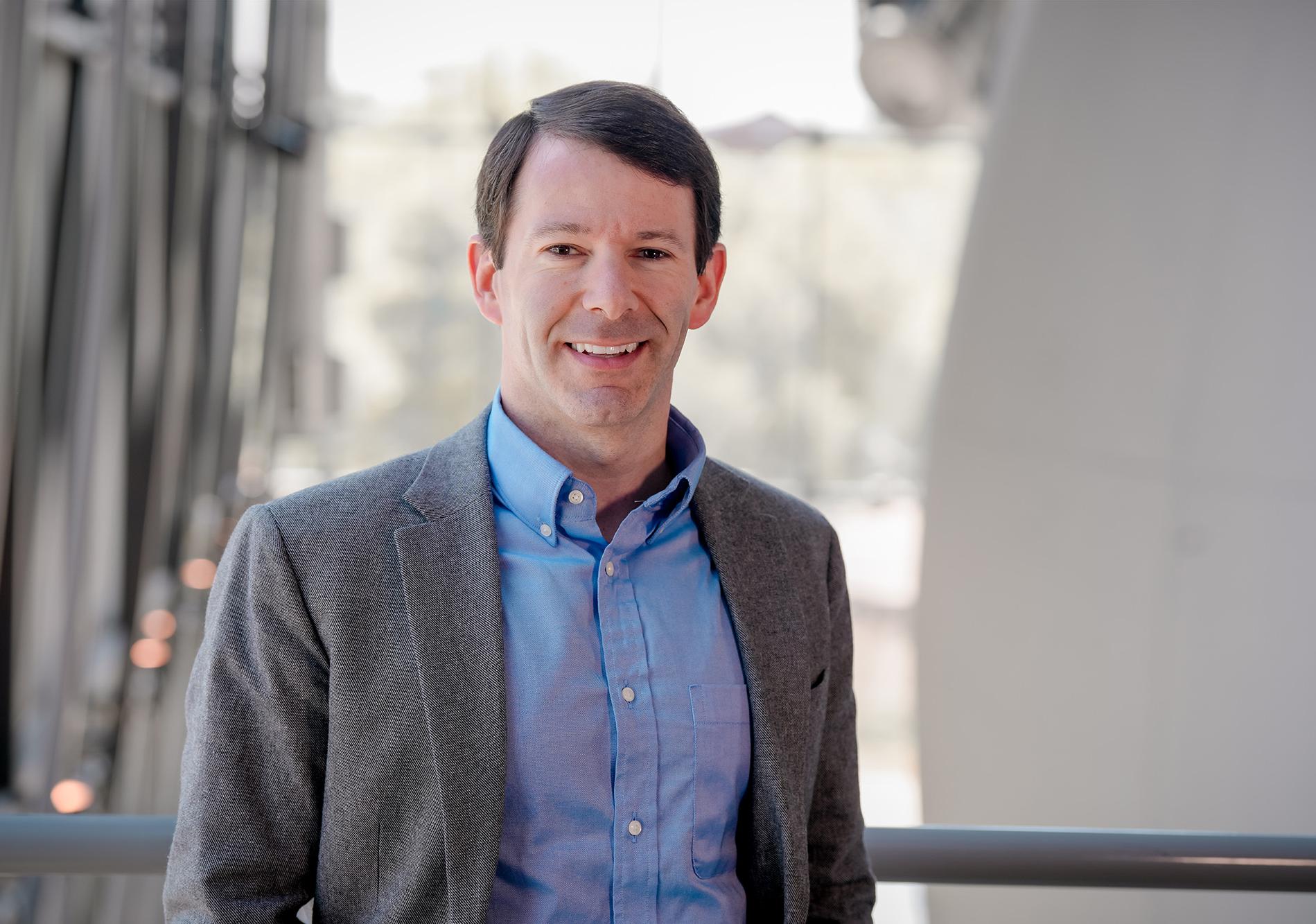 Man in gray suit jacket and blue shirt smiles