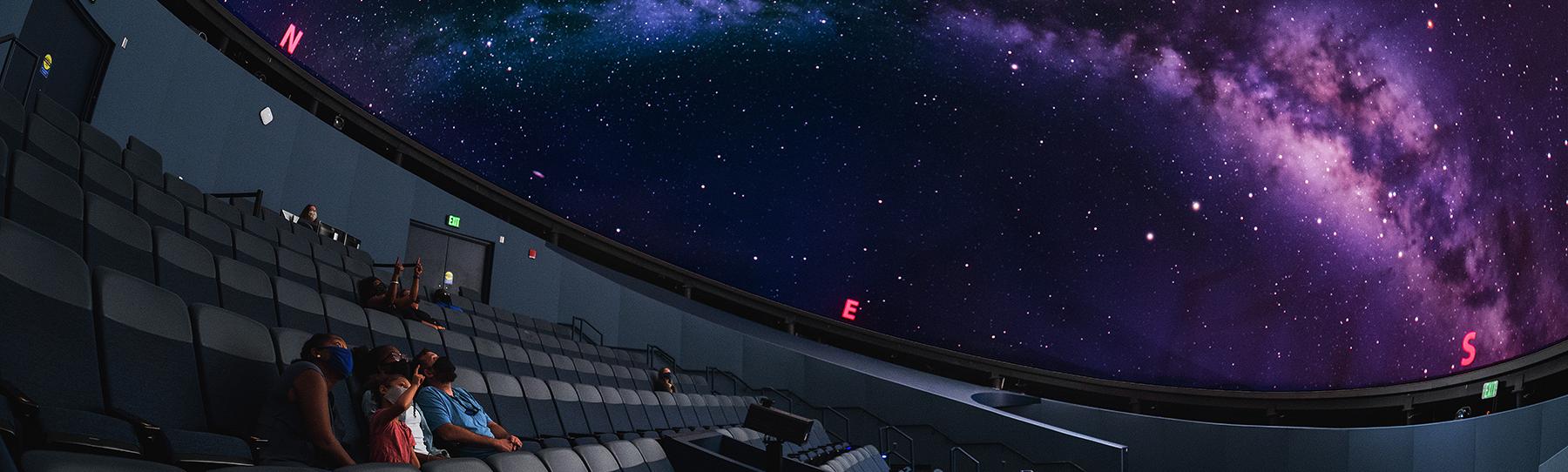 State Museum Planetarium with guests seated and one young girl pointing up at the milky way projected on the dome