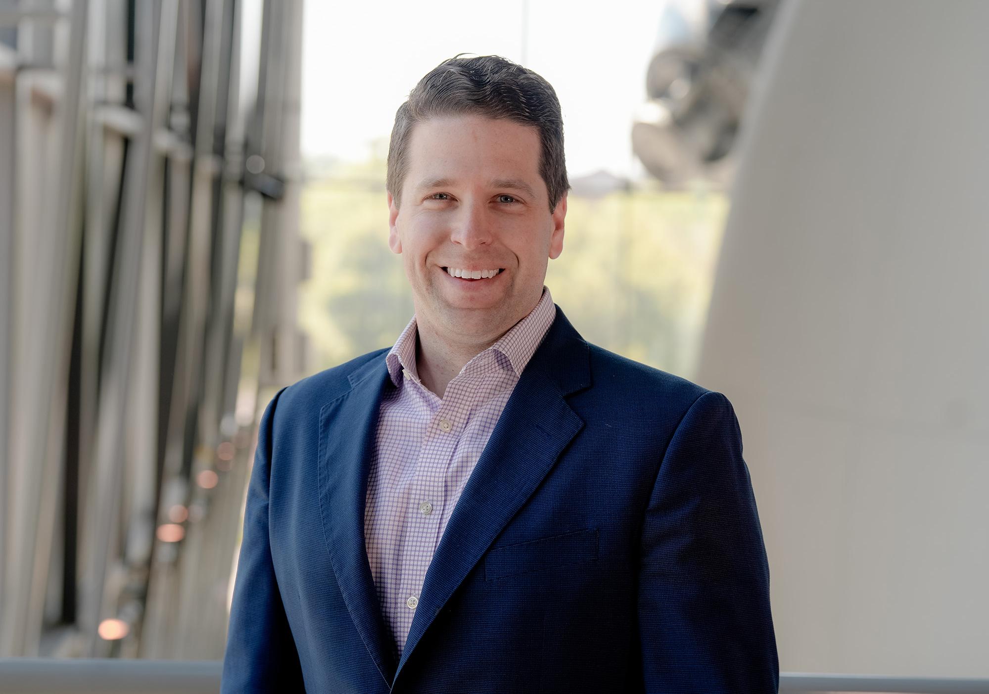 Man navy suit jacket with light red checked shirt smiles