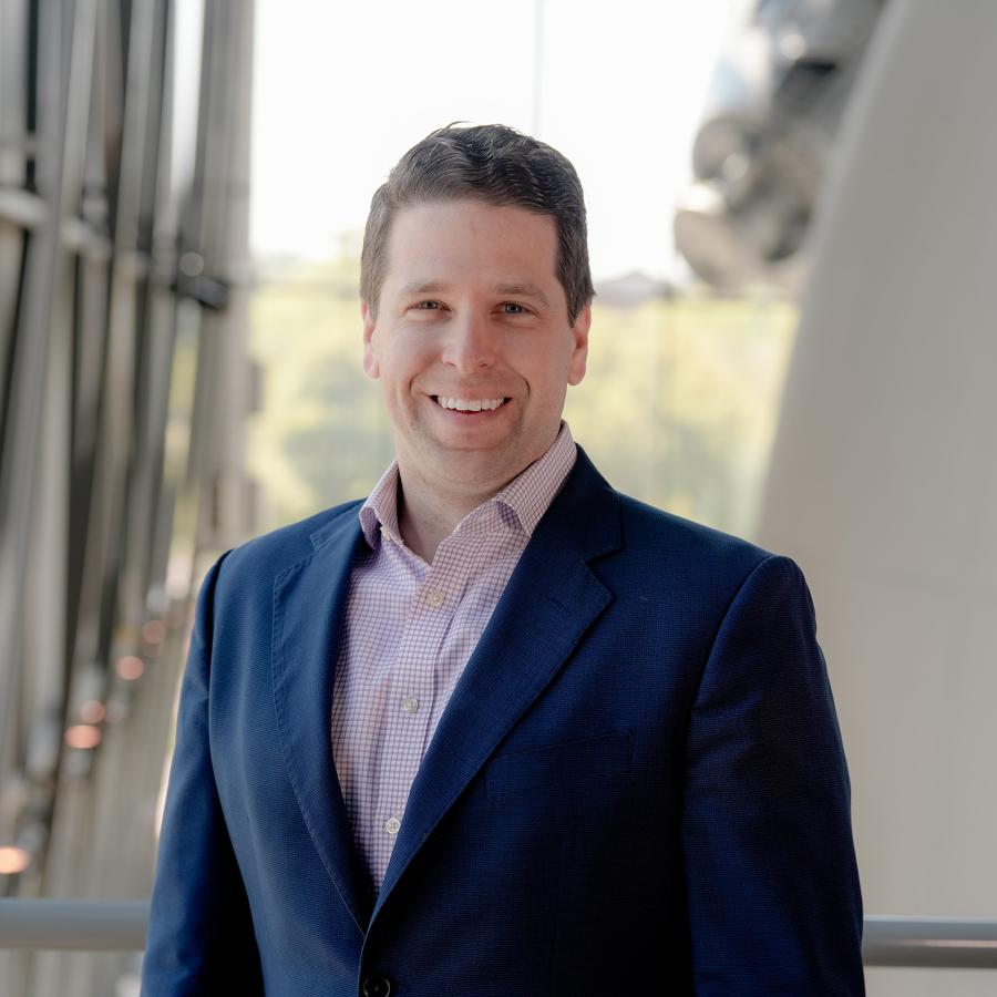 Man navy suit jacket with light red checked shirt smiles