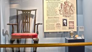 Large, ornate wooden chair with back, arms and scroll feet with red seating cushion