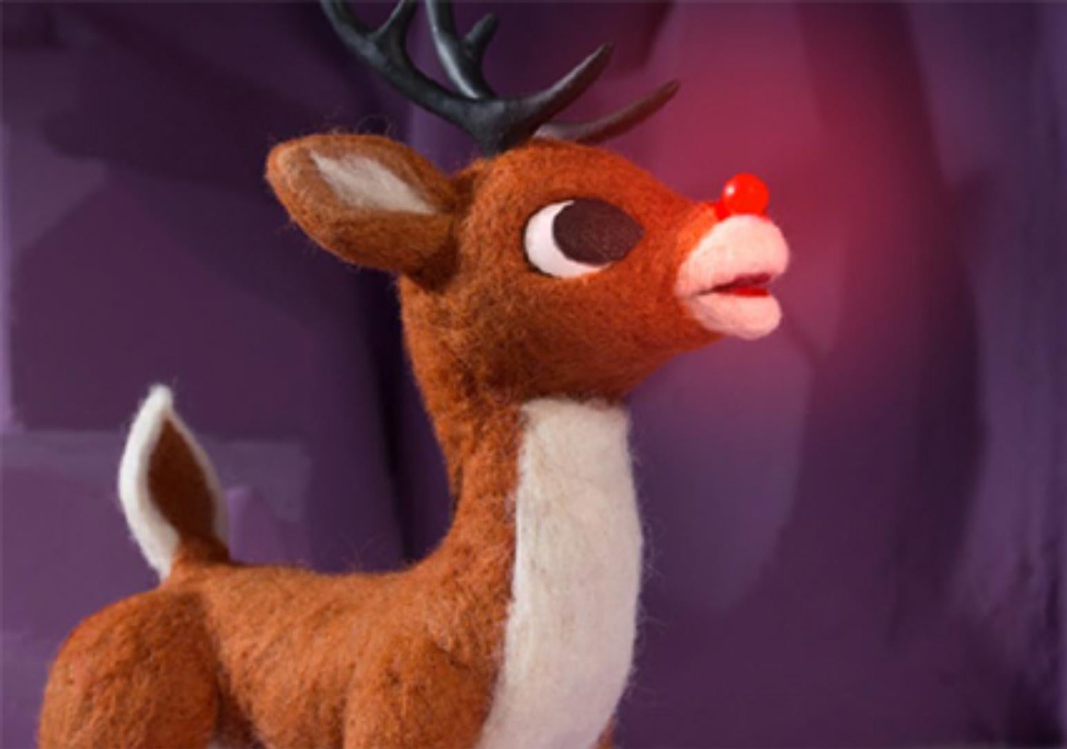 Rudolph the Red Nosed Reindeer with glowing nose stands against a purple background.