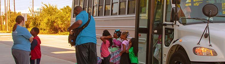 Group of small students and two adults exits a white bus parked next to the South Carolina State Museum