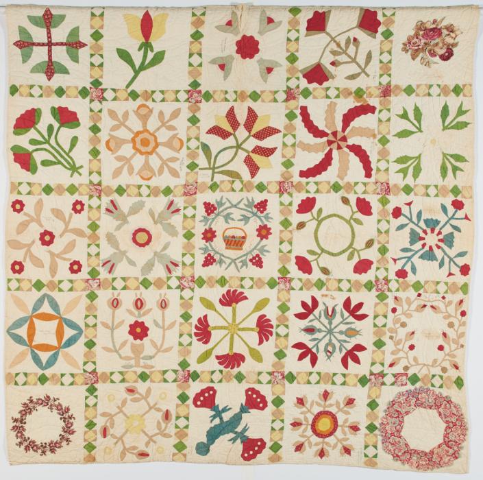 a quilt with green, red and yellow flowers on a cream colored background