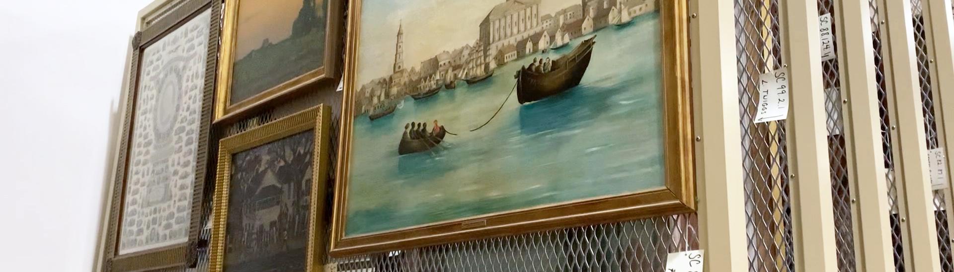 Four framed paintings are mounted on the uppermost section of a rolling rack in the museum's art storage room.