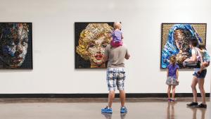 Family looks at 3 pieces of art displayed on a wall, including a portrait of Marilyn Monroe