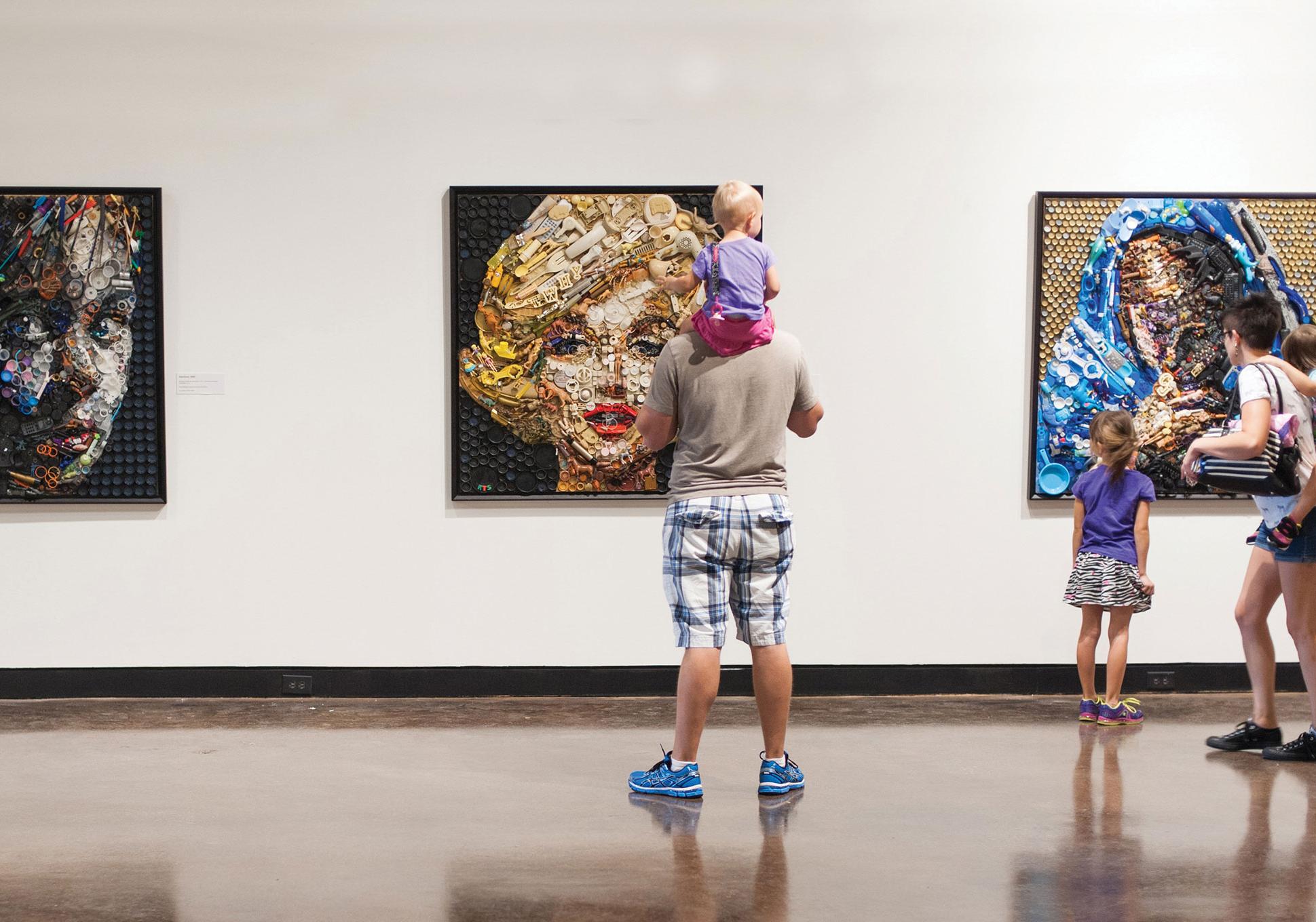 Family looks at 3 pieces of art displayed on a wall, including a portrait of Marilyn Monroe