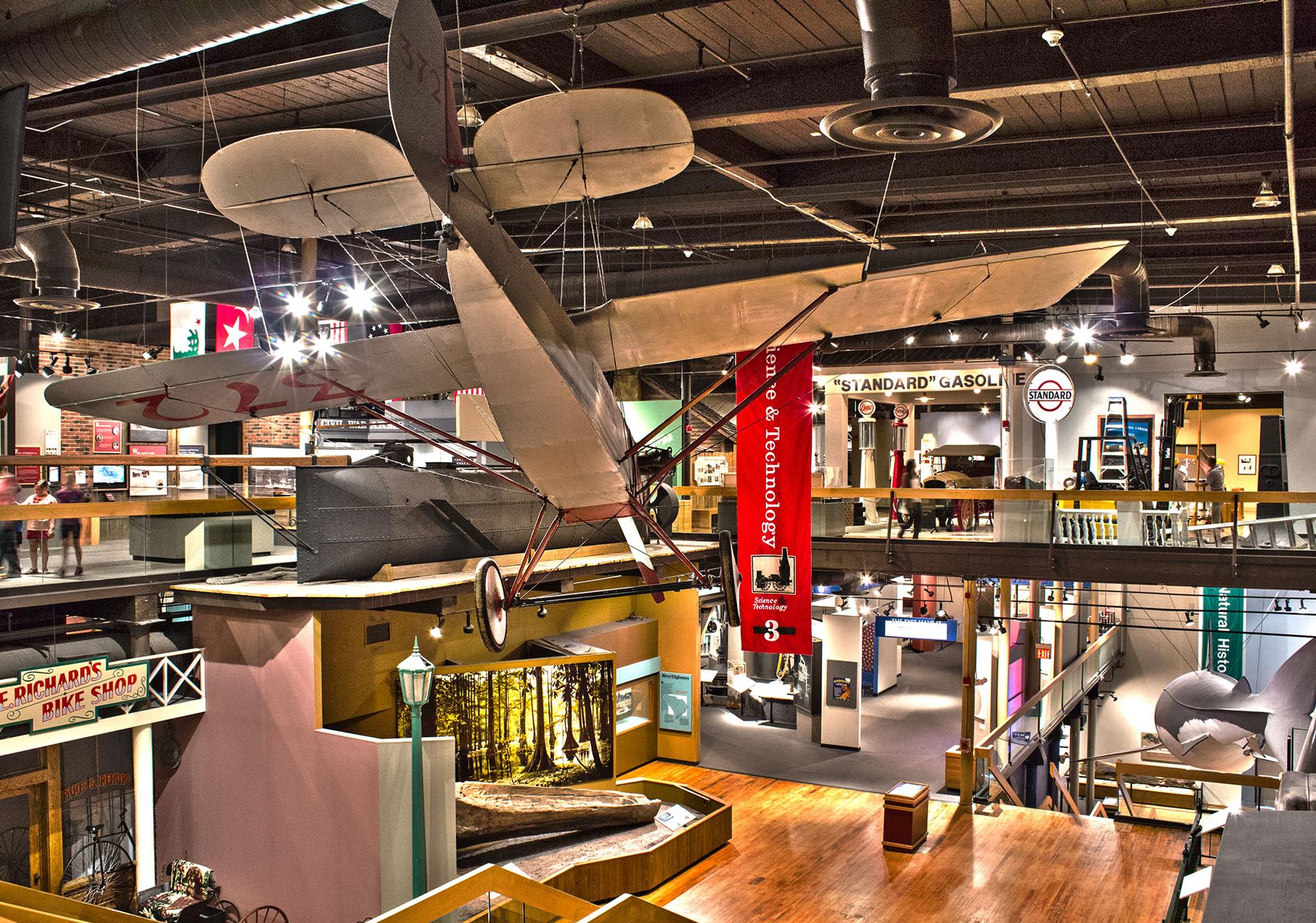 SC State Museum 4th floor exhibit gallery looking down onto the 3rd floor galleries with Clemson plane suspended from ceiling in foreground