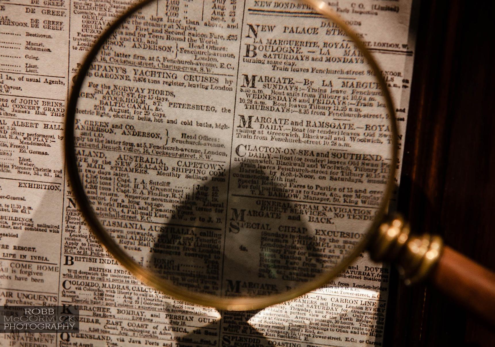 Close up image of magnifying glass with brass rim and a newspaper in the background
