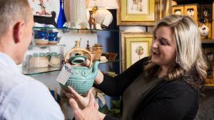 Blonde woman holds up light green ceramic tea pot on sale in the museum store