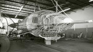 Black and white shows very large metal skeleton of a Megalodon shark in a workshop-like space