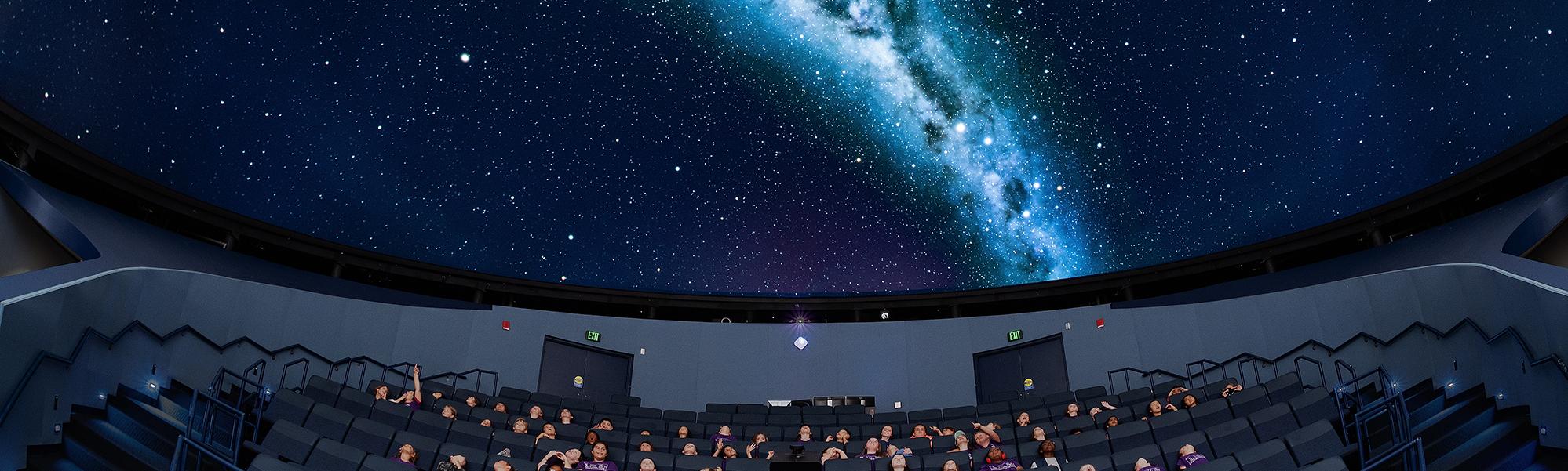 Group of school children sit under the planetarium dome which projects an image of the milky way