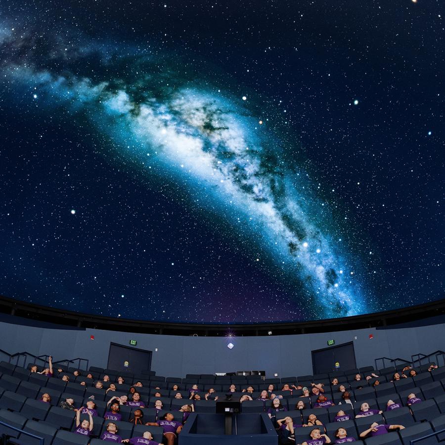 Group of school children sit under the planetarium dome which projects an image of the milky way