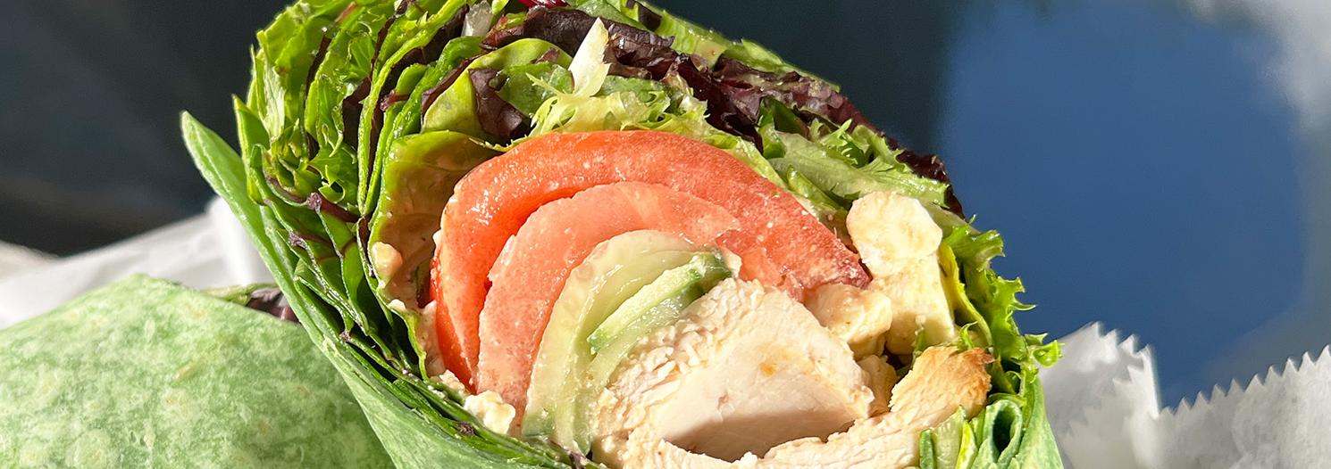 Wrap sandwich cut in half sitting in a dark plastic basket tray with lettuce, tomato, cheese and turkey in a green spinach wrapk