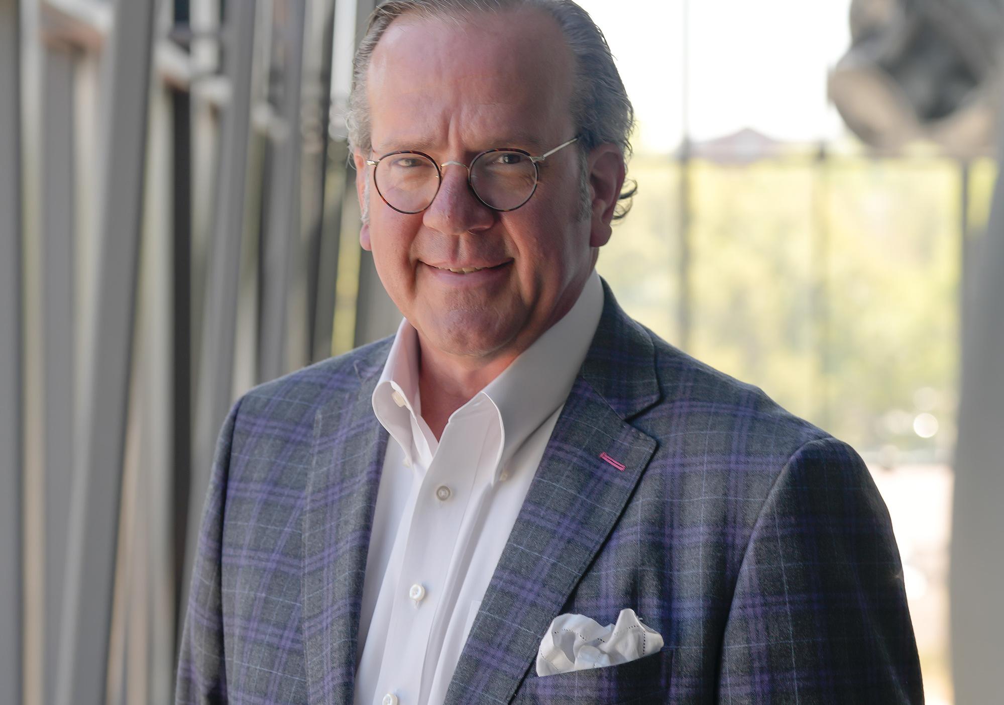 Man in grat suit jacket with white shirt smiles at camera