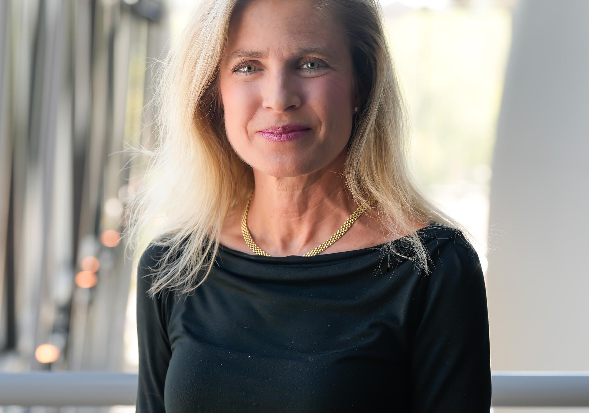 Woman with blonde hair wearing black blouse smiles at camera