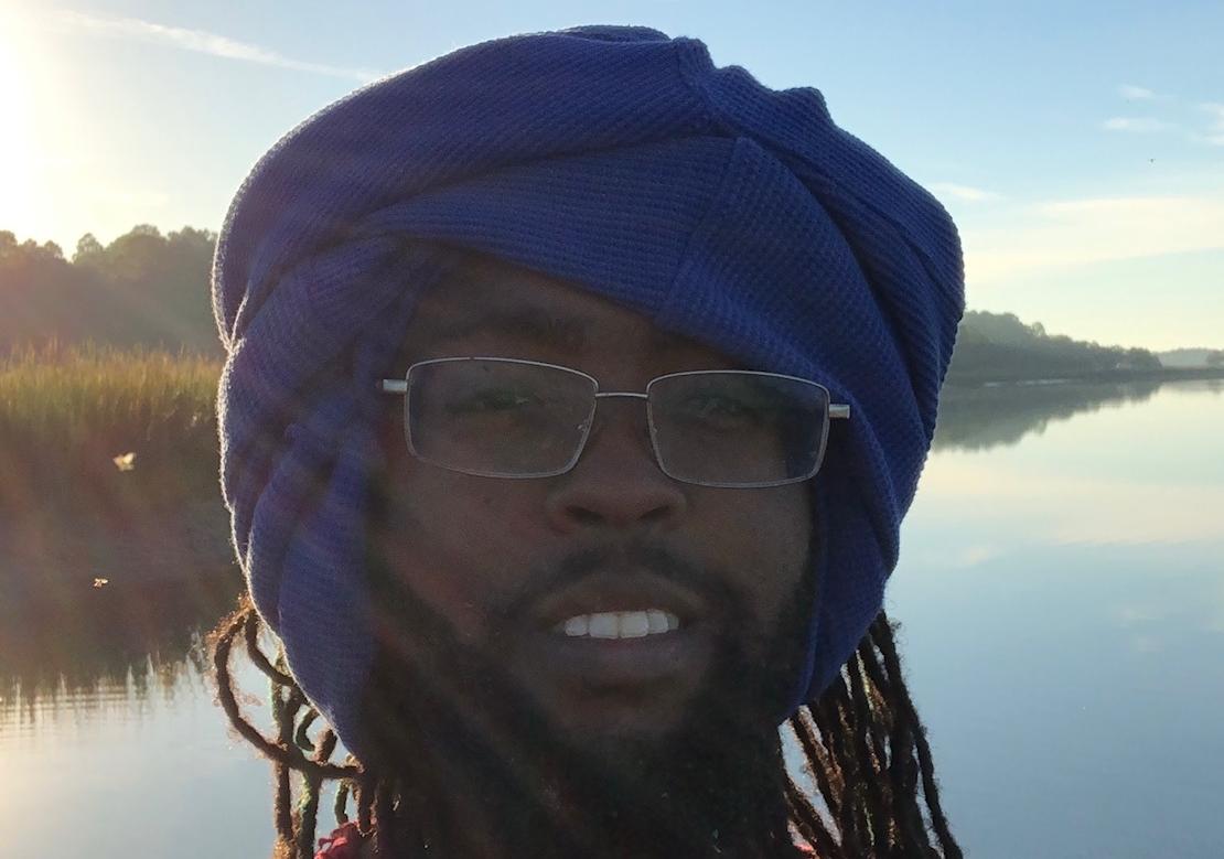 Bald, bearded with  glasses wearing a black hoodie looks down at a bottle of Mr Seafood sauce he holding in his hand 