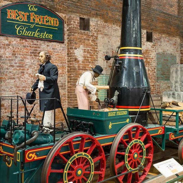 Full size train replica of The Best Friend of Charleston at the State Museum. Shows green train with red wheels and black smoke stack.