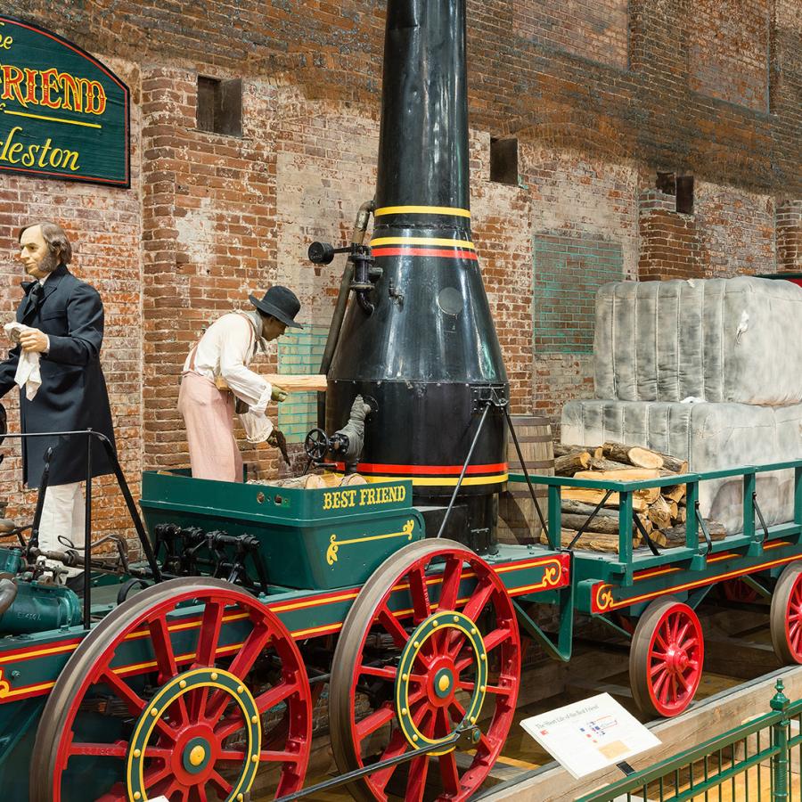 Full size train replica of The Best Friend of Charleston at the State Museum. Shows green train with red wheels and black smoke stack. 