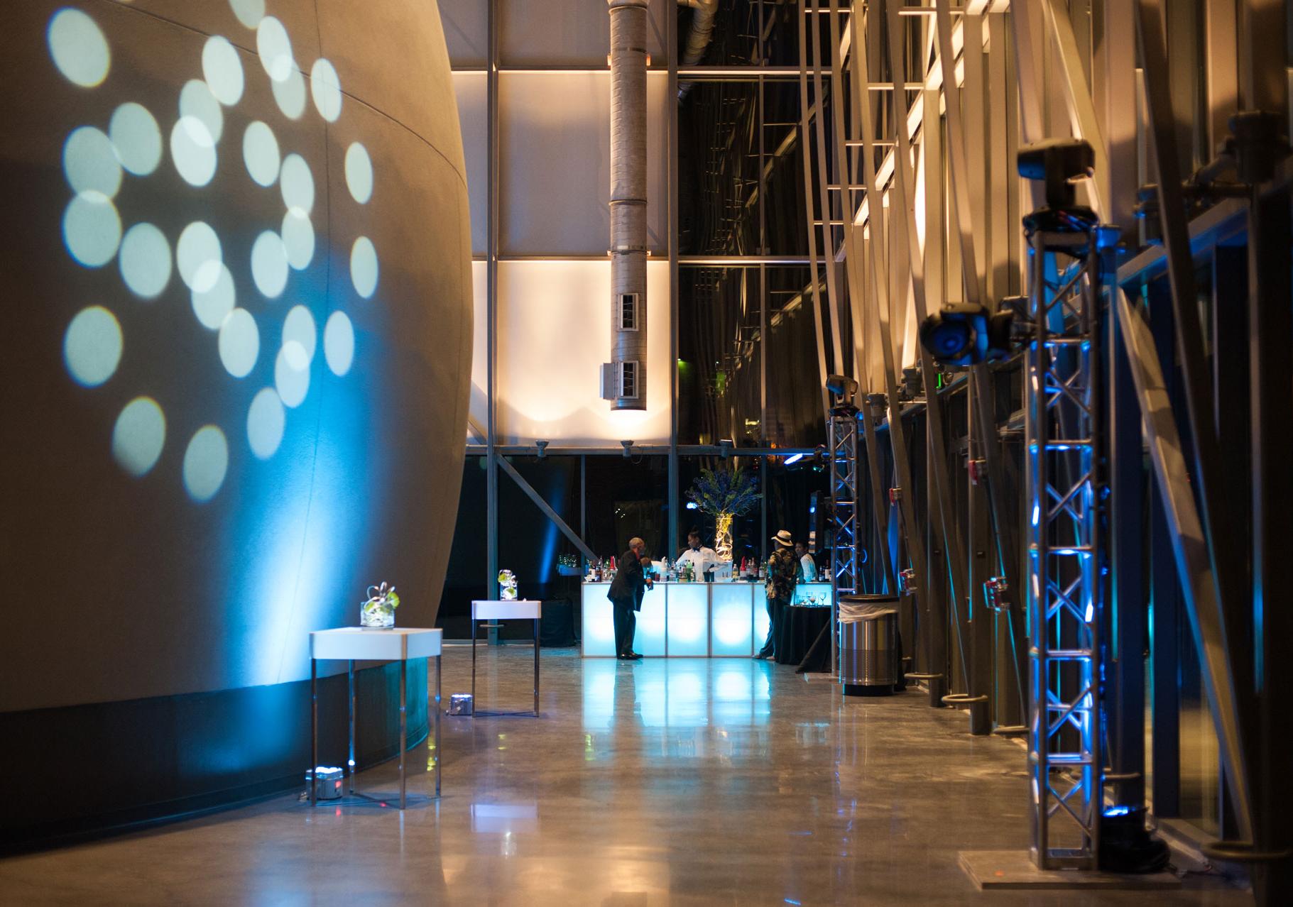 Planetarium lobby during evening reception shows the side of the large dome exterior on the left with circular lights projected on it 