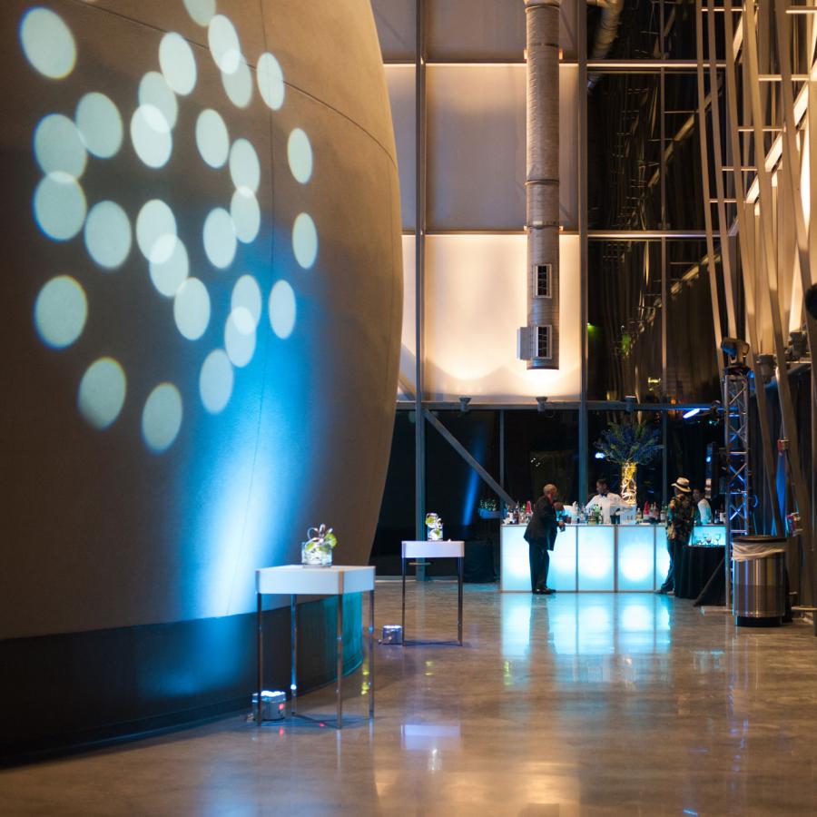 Planetarium lobby during evening reception shows the side of the large dome exterior on the left with circular lights projected on it 