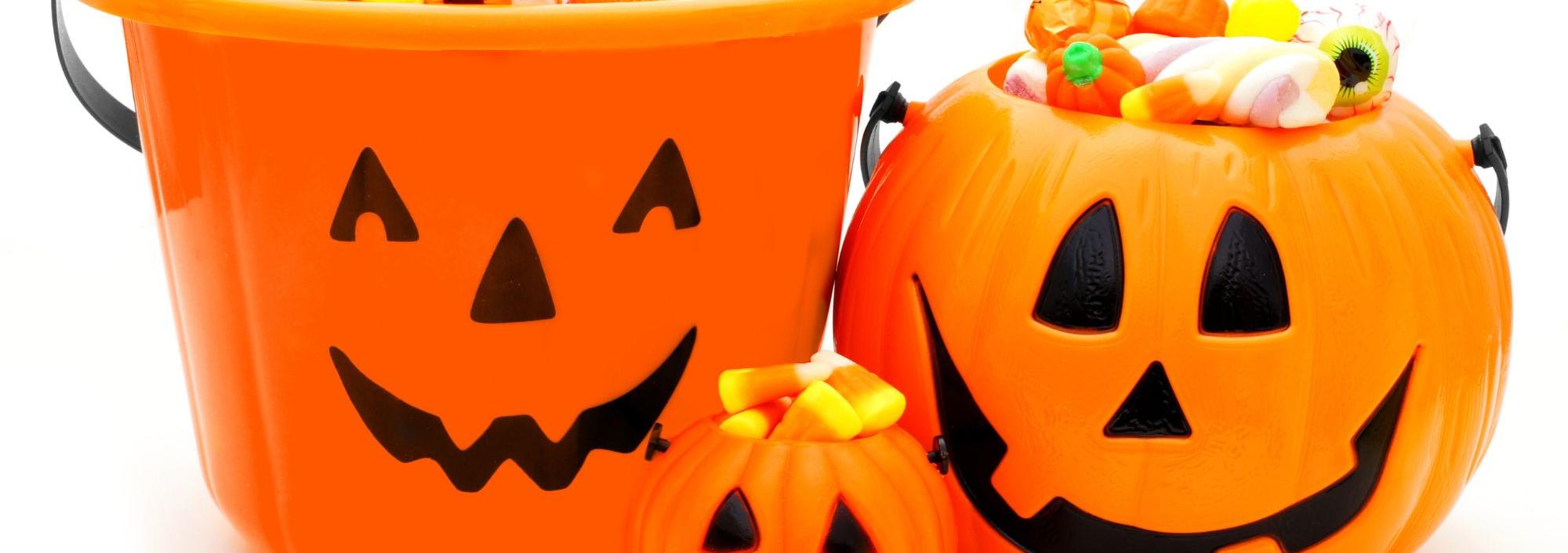 Three orange plastic pumpkin baskets with candy spilling over their brims