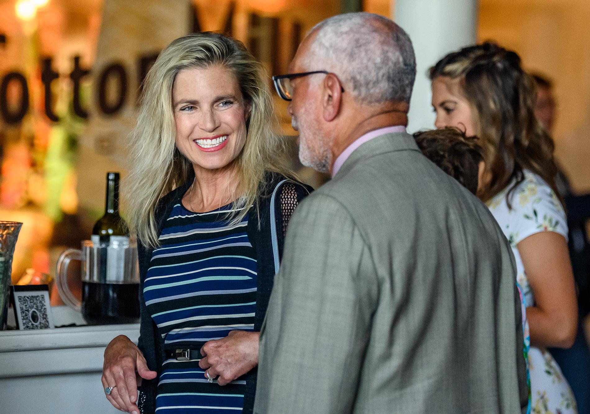 Two reception guests talk with each other with bar setup in the background