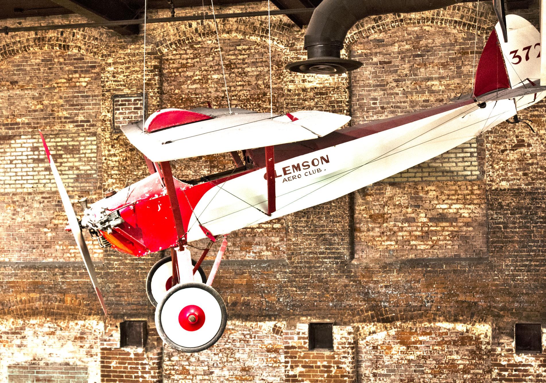 Red and white propeller airplane is suspended from the ceiling on display at the South Carolina State Museum.