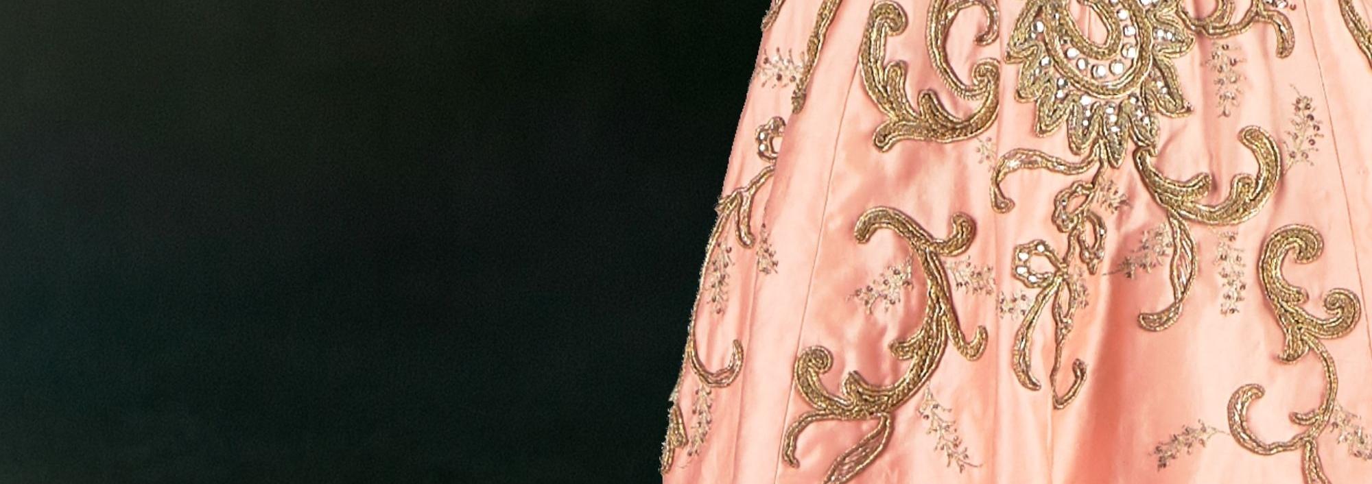 Peach gown detail with intricate gold embroidery on a dark green backdrop