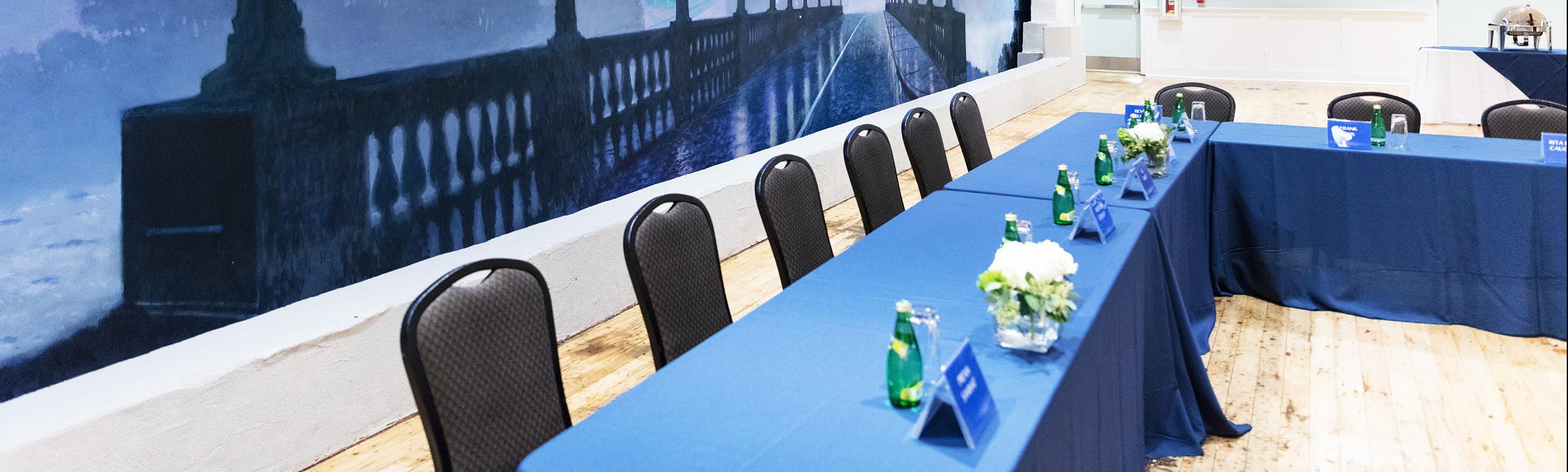 Mural of bridge on left side wall of room with table set up in front with blue table cloth