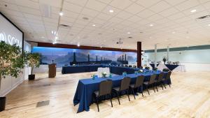 Large room with light colored wooden floor has table set up in u shape facing a large screen on the wall with mural of bridge in the background