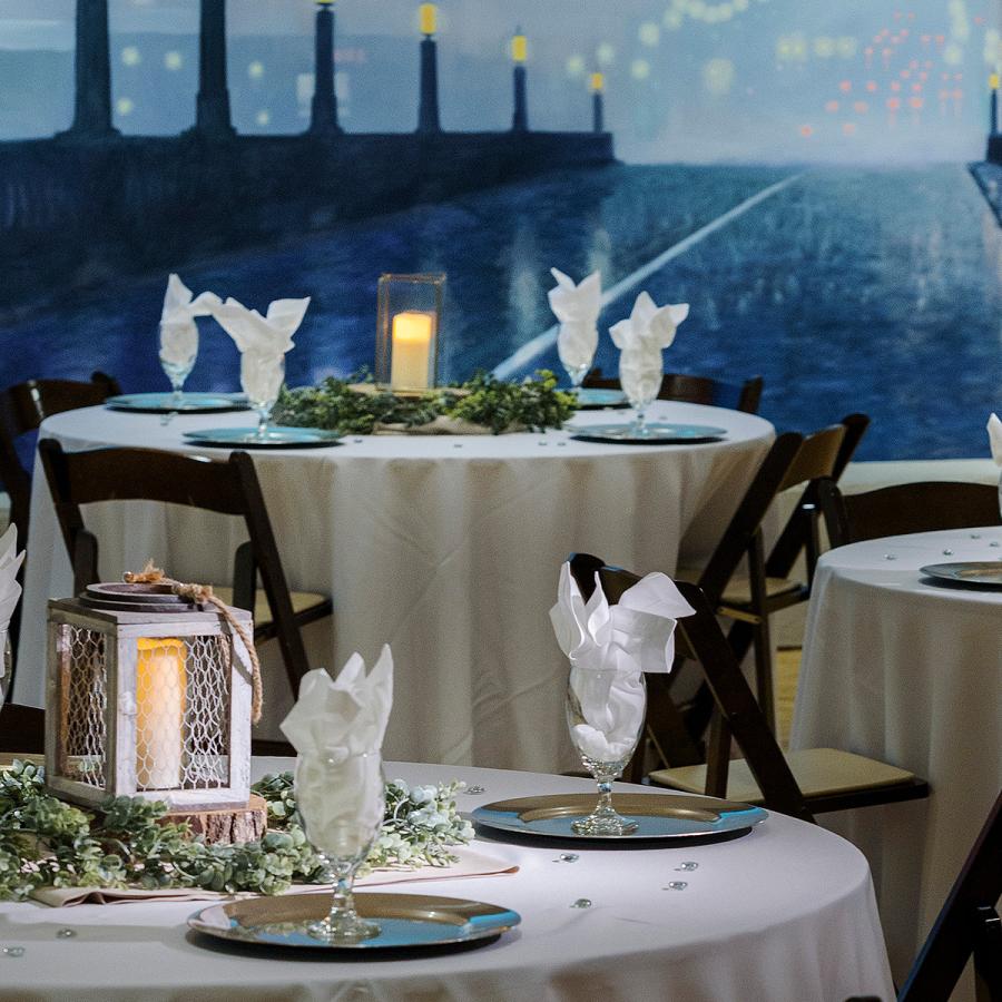 Three formally set table with the white table cloths and napkins with painted mural of bridge in the background