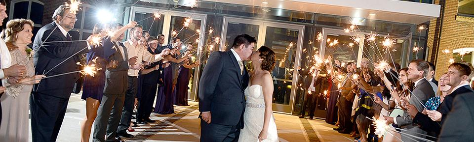 Bride and groom pose at museum entrance at night with guests holding sparklers along either side of the couple