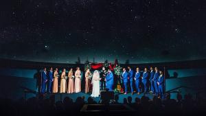 Wedding ceremony in the planetarium with couple flanked by bridesmaids and groomsmen with large projection of a starry night sky behind them.