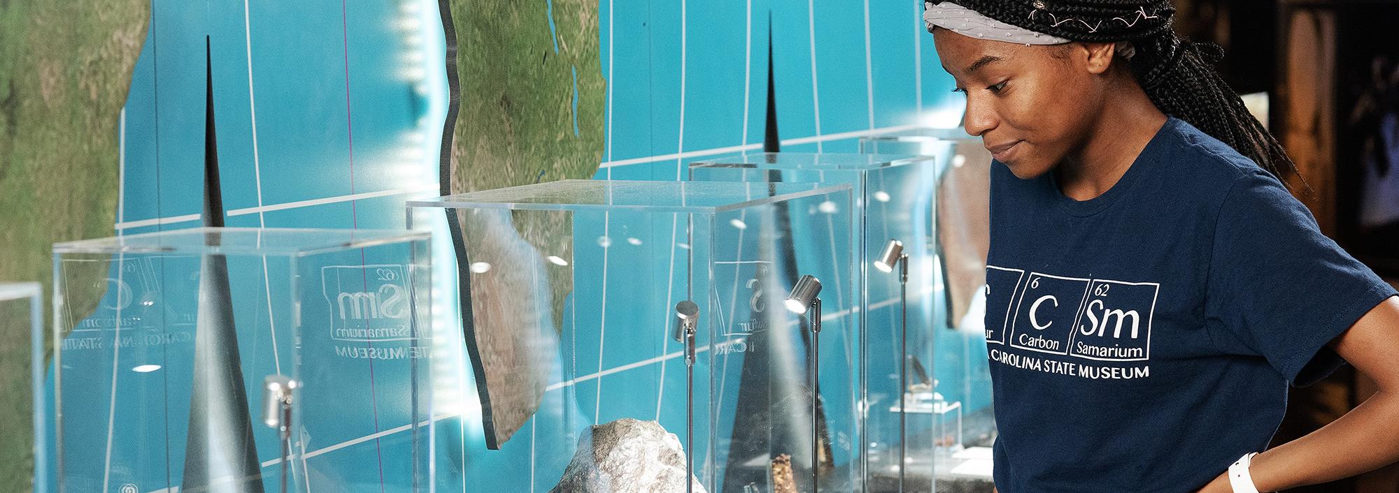 Young woman observes a large gray meteorite in a display case mounted to a wall