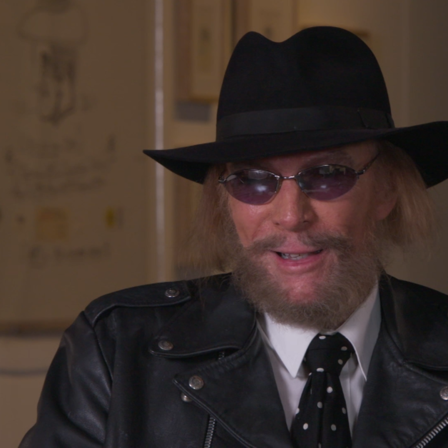 Man in black hat with dark beard and mustache wearing sunglasses and black leather jacket