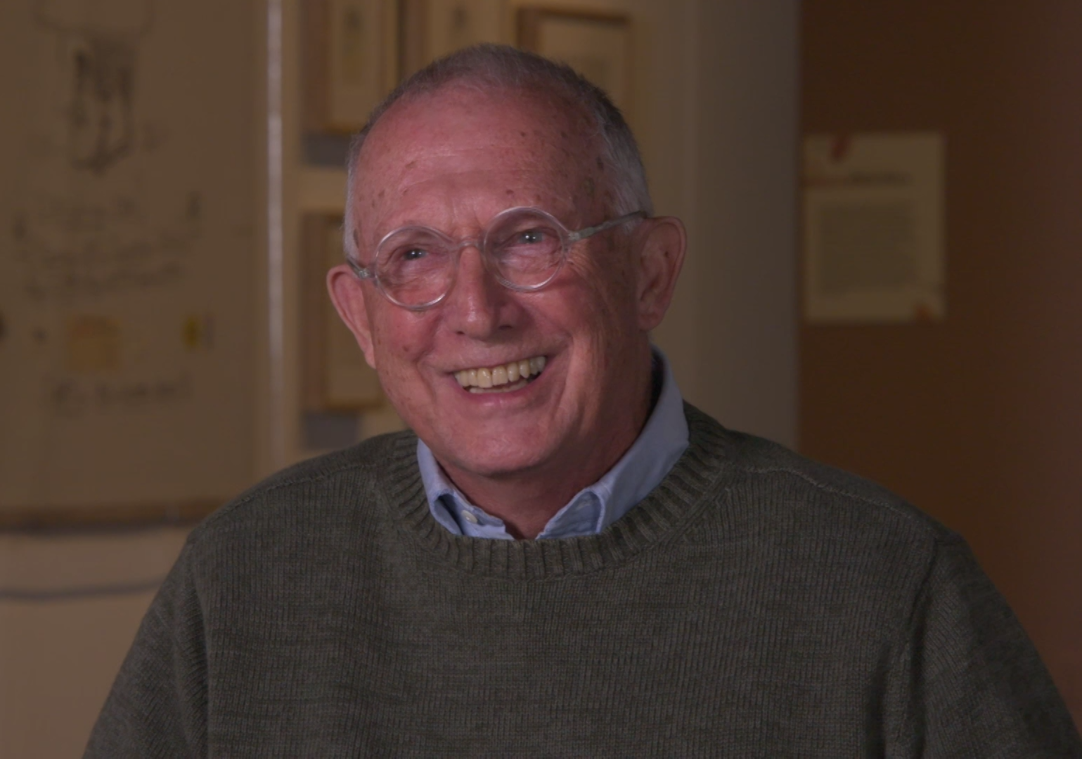 Older man with glasses and wearing a sweater smiles