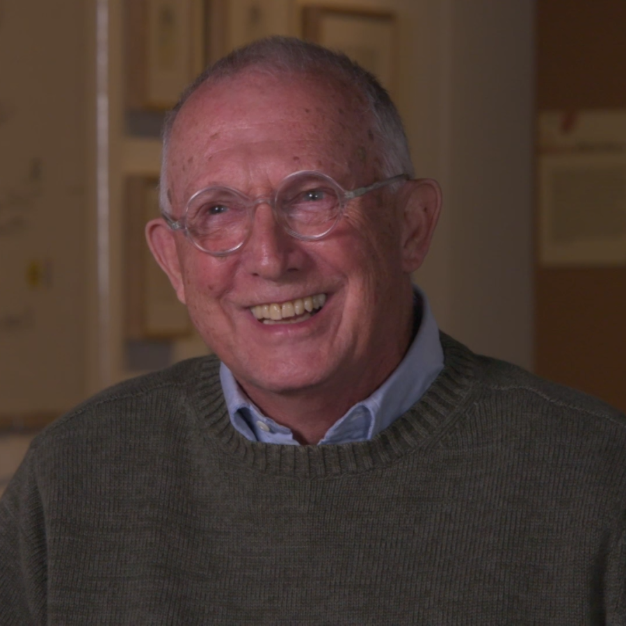 Older man with glasses and wearing a sweater smiles