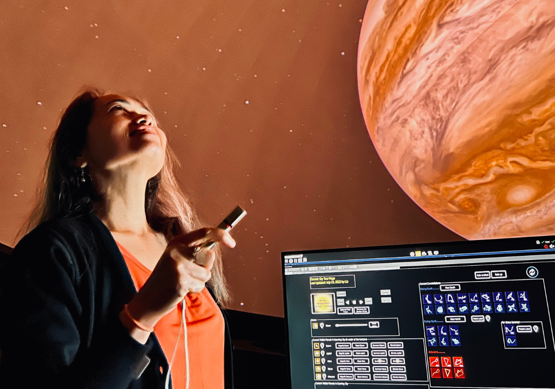 Woman looks up projection of Jupiter on planetarium dome while holding small flashlight
