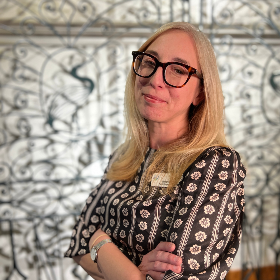 Woman with blonde hair wearing glasses stands 3/4 towards camera with arms crossed