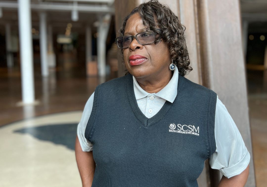 Woman in navy blue vest with museum logo poses for camera