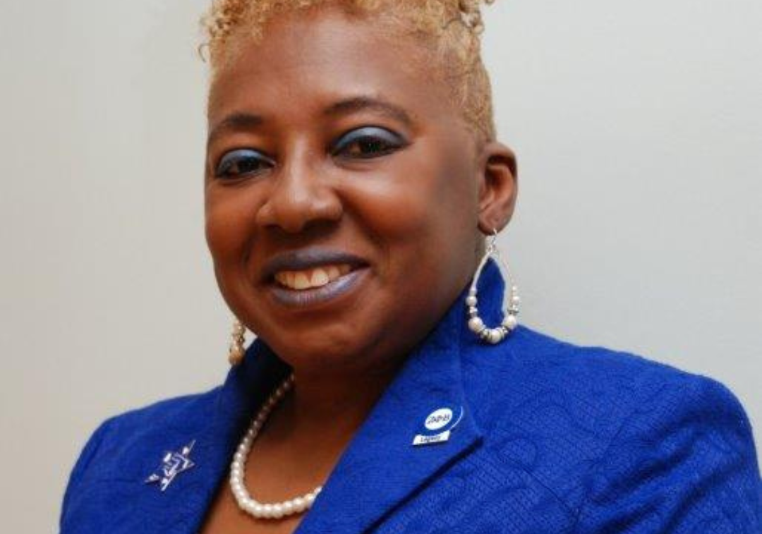 Woman with short blond hair in a sharp blue jacket smiles at camera
