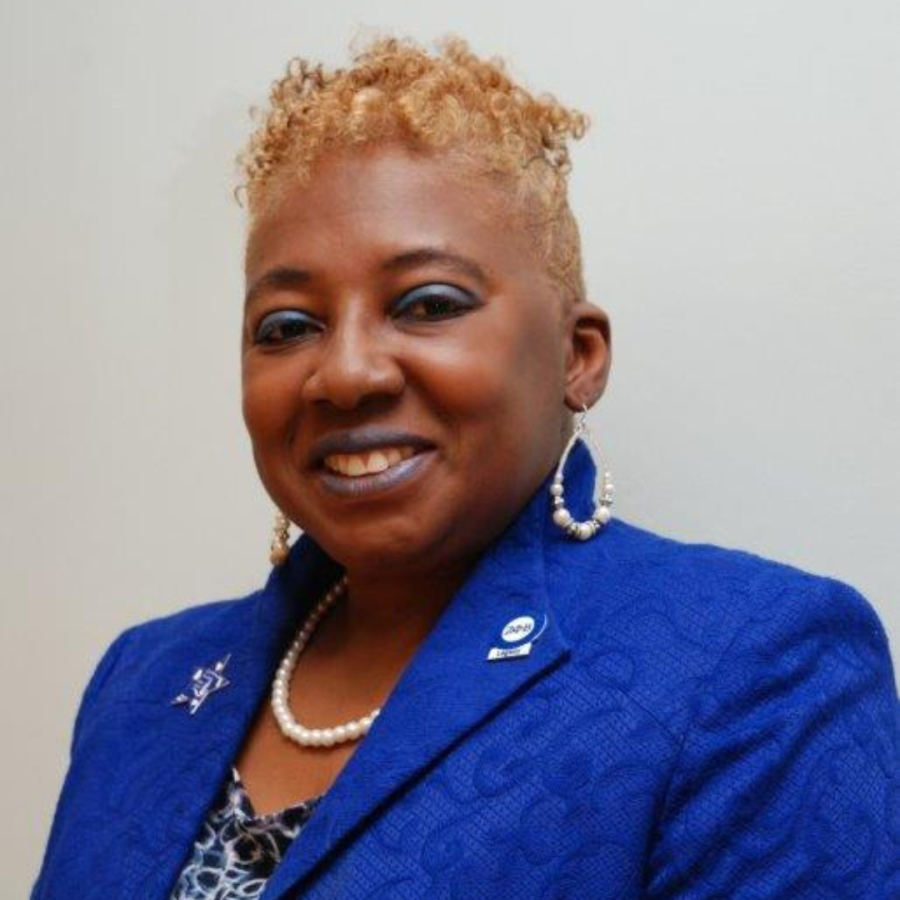 Woman with short blond hair in a sharp blue jacket smiles at camera